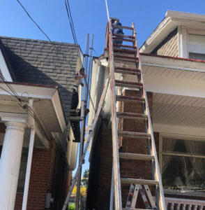 Worker on a ladder performing gutter installation on a residential home, showcasing the importance of proper gutter systems for water drainage and home protection.