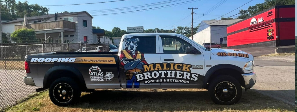 Malick Brothers roofing truck with company branding, featuring a cartoon dog mascot, parked near residential buildings, emphasizing professional roofing services and local presence.