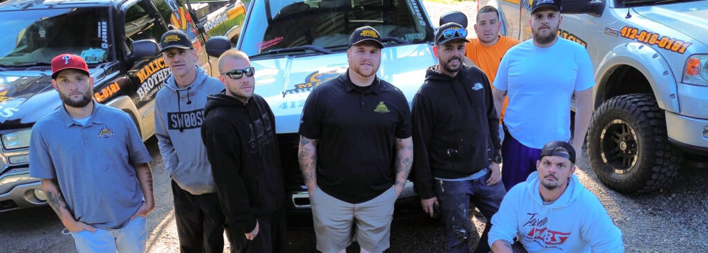 Group of Malick Brothers Exteriors team members posing in front of company trucks, showcasing expertise in roofing and exterior solutions for Pittsburgh's climate.