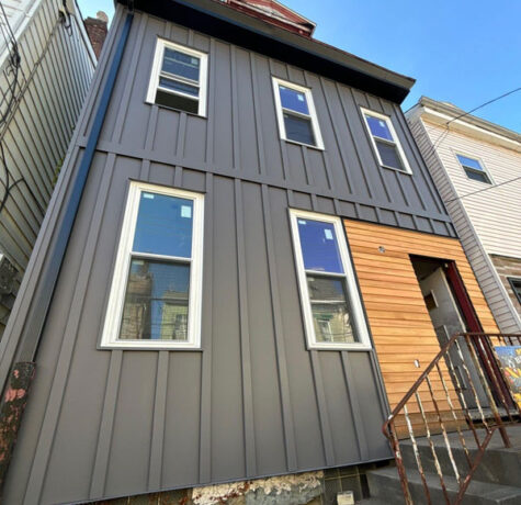 Modern residential building featuring dark gray metal siding and natural wood accents, showcasing energy-efficient exterior solutions relevant to commercial roofing options in Pittsburgh.