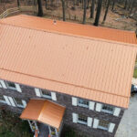 Metal roofing installation on a commercial building in Pittsburgh, featuring a standing seam design and a copper-colored finish, surrounded by wooded area.