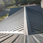 Metal roofing installation viewed from above, showcasing the sloped roof design and surrounding greenery, relevant to Malick Brothers Roofing & Exteriors' community outreach and service offerings.