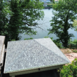 Metal roof installation on a residential property with a scenic view of a river and surrounding trees, highlighting durability and aesthetic appeal in roofing options.