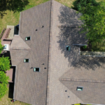 Aerial view of a residential roof featuring multiple slopes, skylights, and surrounding greenery, illustrating effective roof design for energy efficiency and sustainable living.