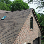 Roof with asphalt shingles and skylight on a historic Pittsburgh property, surrounded by trees, showcasing traditional roofing techniques and modern materials.