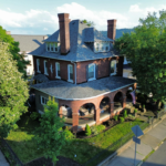 Historic brick home with a slate roof and prominent chimneys, surrounded by greenery, showcasing effective roof ventilation design for energy efficiency and structural integrity.