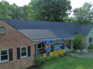 Malick Brothers Exteriors banner on a residential roof with workers, showcasing roofing services in Pittsburgh.