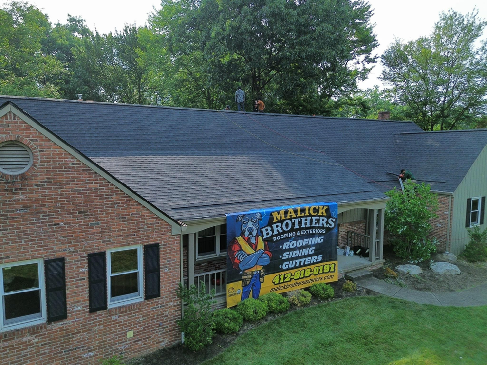 Newly installed asphalt shingles on a residential home with Malick Brothers Exteriors sign prominently displayed in front, showcasing high-quality roofing work.