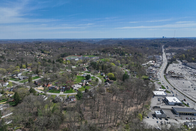 Aerial view of Ross Township showing residential areas, trees, and nearby commercial buildings, emphasizing the community affected by recent storm damage to roofs.