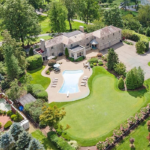 Aerial view of a residential property with a swimming pool, surrounded by lush greenery and landscaped gardens, relevant to roofing maintenance discussions for homeowners in Cheswick.