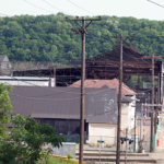 Industrial building with a damaged roof and utility poles, surrounded by greenery, representing potential gutter issues and maintenance needs in home exteriors.