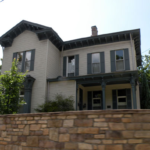 Historic home with a well-maintained roof and decorative trim, surrounded by greenery and a stone wall, illustrating the importance of regular roof inspections and maintenance in Brackenridge.