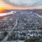 Aerial view of Pittsburgh's West End neighborhood at sunset, showcasing residential rooftops and surrounding landscape, emphasizing the importance of roof maintenance to prevent wildlife damage.