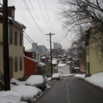 Snow-covered street in Pittsburgh's South Side, showcasing residential houses and rooftops, emphasizing winter conditions relevant to roof maintenance tips.