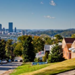 Pittsburgh skyline view from Hazelwood neighborhood with residential houses and greenery in the foreground.