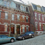 Historic brick buildings in Crafton Heights with parked cars along a cobblestone street, emphasizing the neighborhood's architectural style relevant to local roofing maintenance.