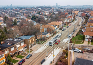 Aerial view of a suburban neighborhood with residential buildings, a streetcar on tracks, and parked cars, illustrating urban infrastructure relevant to roofing and building permit discussions.