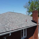 Roofing installation featuring a well-maintained asphalt shingle roof on a residential home, highlighting proper installation techniques and materials for durability, set against a clear blue sky.