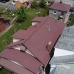 Aerial view of a residential roof with a new metal roofing system, showcasing quality craftsmanship and contrasting materials in the surrounding neighborhood, emphasizing the importance of choosing reliable roofing solutions.