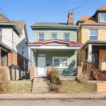 Green two-story house with brick veneer accents, showcasing a blend of traditional and modern architectural styles, located in a residential neighborhood.