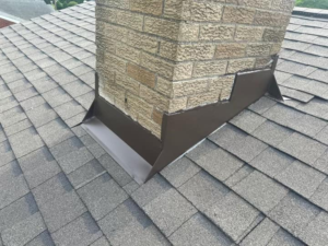 Chimney flashing installation on a sloped roof with asphalt shingles, showcasing waterproofing techniques relevant to commercial roofing practices in Pittsburgh.