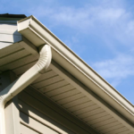 Gutter system on residential roofing with clear blue sky, illustrating aspects of exterior maintenance relevant to EPDM roofing solutions.