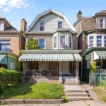 Ranch-style home in Pittsburgh featuring a green and gray exterior, front porch with awning, and well-maintained landscaping, illustrating suitable roofing options for local architecture.