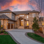 Luxurious estate with elegant stone architecture, landscaped front yard, and dramatic sunset sky, emphasizing premium roofing potential for upscale properties in Fox Chapel.