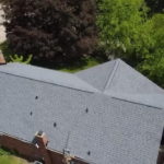 Aerial view of a residential roof with grey shingles, surrounded by lush green trees, illustrating roofing maintenance in Pittsburgh.