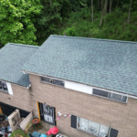 Aerial view of a residential building with a well-maintained asphalt shingle roof, surrounded by greenery, highlighting the importance of roof integrity and maintenance.