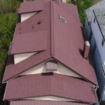 Aerial view of a residential roof with a reddish-brown shingle design, showcasing structural features and adjacent homes, emphasizing the importance of roof maintenance and storm-proofing.