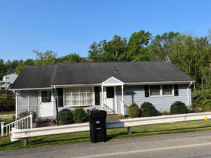 House with a black trash can in front, featuring a sloped roof and architectural shingles, surrounded by greenery, illustrating residential roofing options in Pennsylvania.
