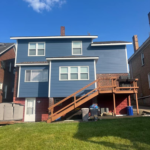 Two-story blue house with a wooden deck and grassy yard, showcasing exterior features relevant to roofing and siding discussions.
