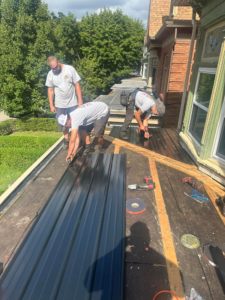 Team of roofers installing metal roofing panels on a residential building, showcasing proactive maintenance and craftsmanship in Pittsburgh.