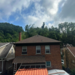 Roof of a residential building with brown shingles, brick exterior, and surrounding trees under a cloudy sky, illustrating the context of professional roof leak repair services.