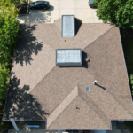 Aerial view of a residential roof featuring two skylights, surrounded by trees, emphasizing the importance of roof maintenance and gutter repairs for homeowners.