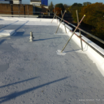 Flat commercial roof with visible drainage pipe and scaffolding, showcasing proper maintenance to prevent ponding water, emphasizing the importance of roof care and drainage systems.