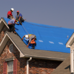 Roofers installing a blue tarp on a residential roof, emphasizing the importance of roof inspections and maintenance for homeowners in Pittsburgh.
