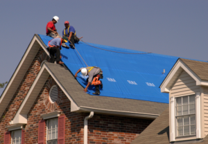 Roofing contractors performing emergency tarp repairs on a residential roof after storm damage, emphasizing immediate protection and mitigation strategies.