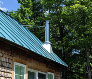 Metal roof installation on a commercial building with chimney, surrounded by trees and blue sky, highlighting durability and weather resistance.