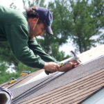 Worker installing roofing materials on a sloped roof, demonstrating home improvement techniques related to gutter installation.