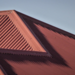 Close-up view of a corrugated metal roof with a red finish, showcasing the texture and design features relevant to durable roofing solutions.