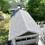 Aerial view of a well-maintained garage roof with asphalt shingles, surrounded by greenery, emphasizing the importance of roof inspection and maintenance for homeowners.