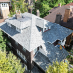 Aerial view of a residential roof with a new slate roofing installation, surrounded by trees and neighboring homes, emphasizing the importance of roof maintenance and quality roofing solutions.