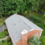 Aerial view of a residential home in Pittsburgh featuring a durable asphalt roof, surrounded by greenery, emphasizing the importance of quality roofing for longevity in challenging weather conditions.