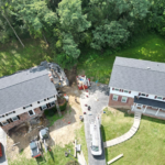Aerial view of two homes with new roofing installations, surrounded by greenery and construction equipment, highlighting the importance of professional roof inspections and maintenance by Malick Brothers Exteriors.