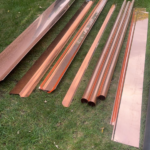 Copper gutter materials arranged on grass, showcasing various profiles and components for high-quality roofing solutions.