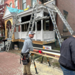 Worker installing copper gutters on a historic home with scaffolding and ladders in the background, showcasing exterior home improvement by Malick Brothers Exteriors.