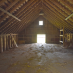 Interior of an empty barn with exposed wooden beams and a door leading outside, illustrating the importance of proper roofing and maintenance to prevent water damage.