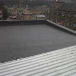 Flat roofing system with a sloped edge overlooking Pittsburgh's historic architecture, highlighting roofing solutions for local weather challenges.